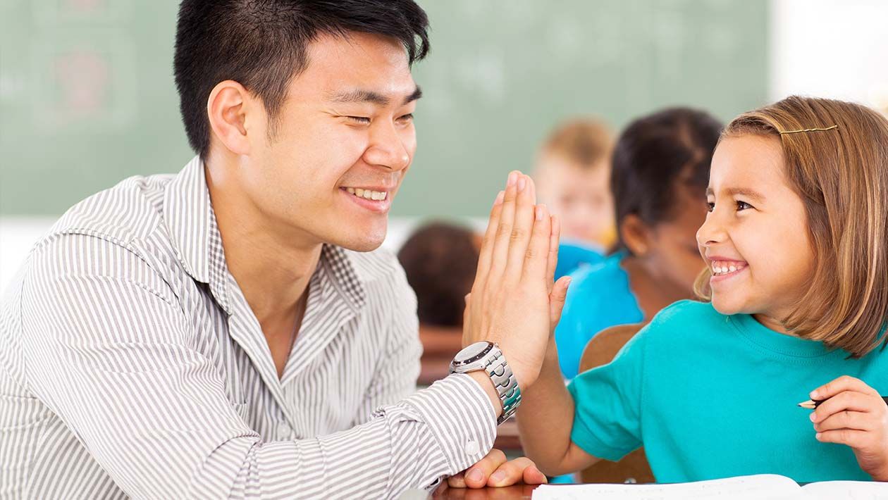 Girl high fiving teacher in the classroom while working on school work