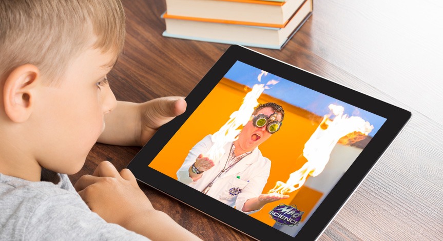 Boy looking at ipad with a mad science instructor on the screen performing with fire on both hands.